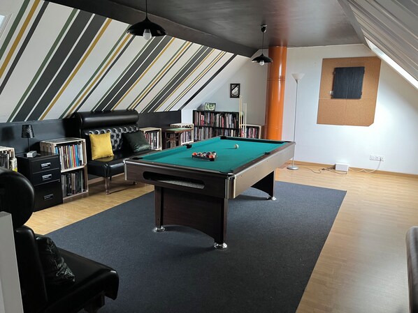 Une pièce comprenant une table de billard, un canapé, une bibliothèque et un plafond à pente.