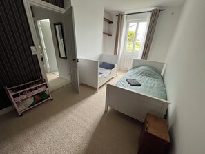 Une chambre avec un lit simple, une petite table de chevet, une armoire et une porte donnant sur une autre pièce.