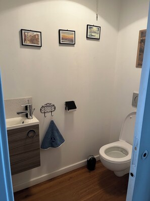 Kylpyhuone, jossa on wc, pesuallas ja kolme kehystettyä kuvaa seinällä.