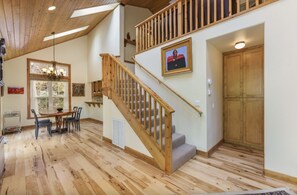 Una habitación amplia con una escalera de madera, un comedor con mesa y sillas, y una gran puerta de madera.