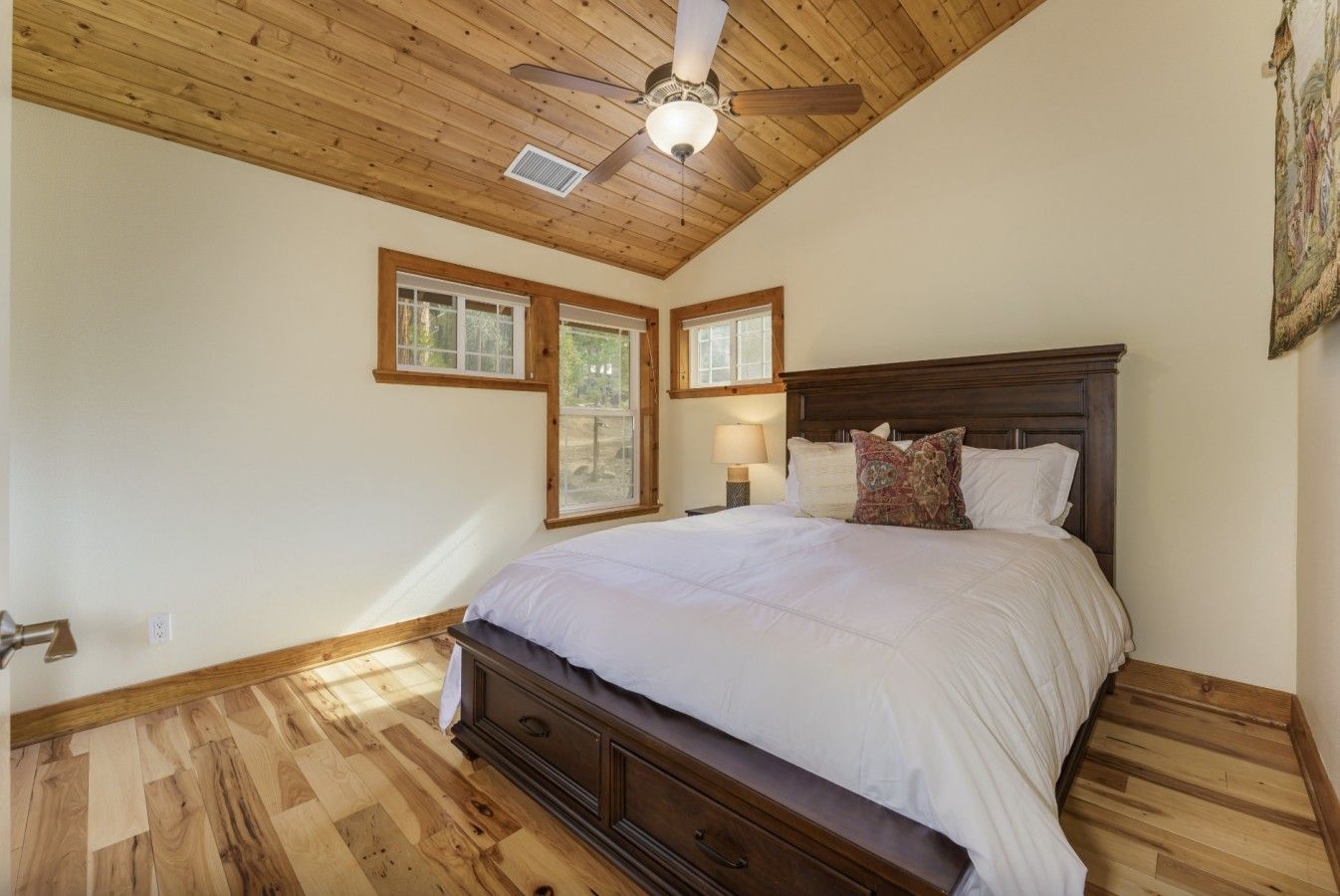 A bedroom with a wooden ceiling, a bed with white bedding, and two windows.