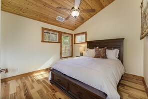 Un dormitorio con techo de madera, una cama con ropa de cama blanca y dos ventanas.