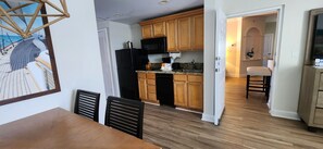 Une cuisine moderne avec des meubles en bois, un réfrigérateur noir et un coin repas comprenant une table et des chaises en bois.