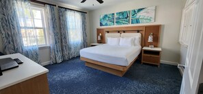 Une chambre d’hôtel avec un lit, des tables de chevet, un bureau et une fenêtre avec des rideaux.