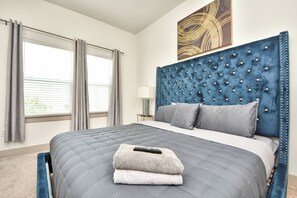 A bedroom with a large bed, a headboard with buttons, a remote control, and a window with curtains. - 1800 Central Pine St (Montgomery)