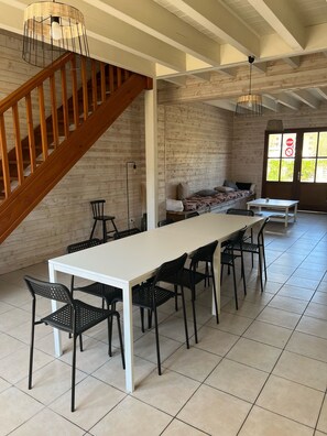 Une pièce spacieuse avec une longue table blanche, des chaises noires, un escalier en bois et un mur en briques.