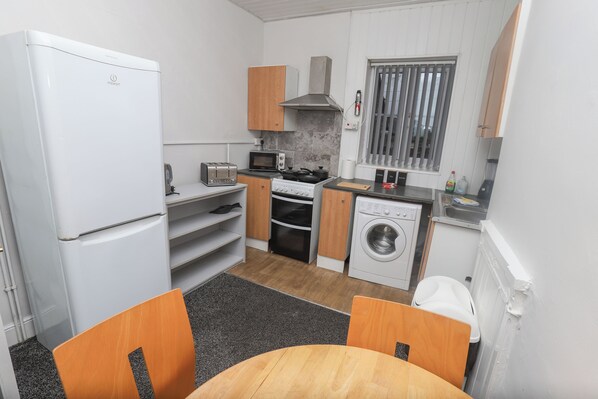 A compact kitchen with a refrigerator, microwave, stove, and washing machine. - Prime Location 3 Bedroom Apartment Central (Middlesbrough)