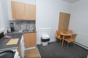 A compact kitchen with wooden cabinets, a sink, a small dining table with chairs, and a trash bin. - Prime Location 3 Bedroom Apartment Central (Middlesbrough)