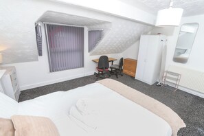 Ein Schlafzimmer mit Bett, Schreibtisch, Stuhl, Kleiderschrank und einem Fenster mit Vorhängen.