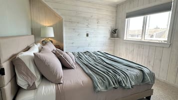 Una camera da letto con un letto, cuscini, una lampada da comodino, una finestra e una pianta.