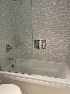 Een badkamer met een douchecabine, een wit bad en toiletartikelen op een plank.