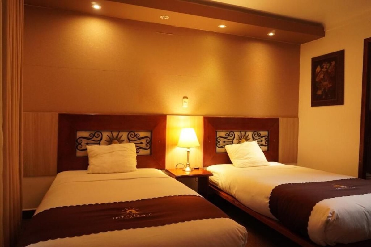 A hotel room with two beds, a nightstand with a lamp, and a painting on the wall.