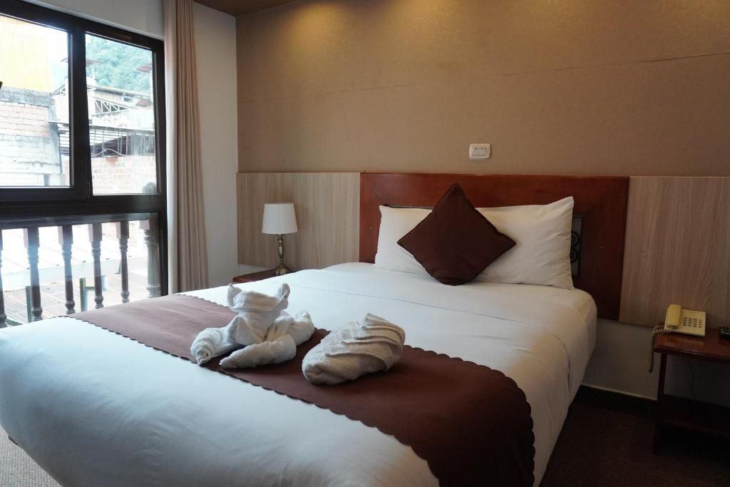 A hotel room with a large bed, a bedside telephone, and a window with a view of buildings outside.