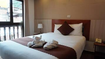A hotel room with a large bed, a bedside telephone, and a window with a view of buildings outside.