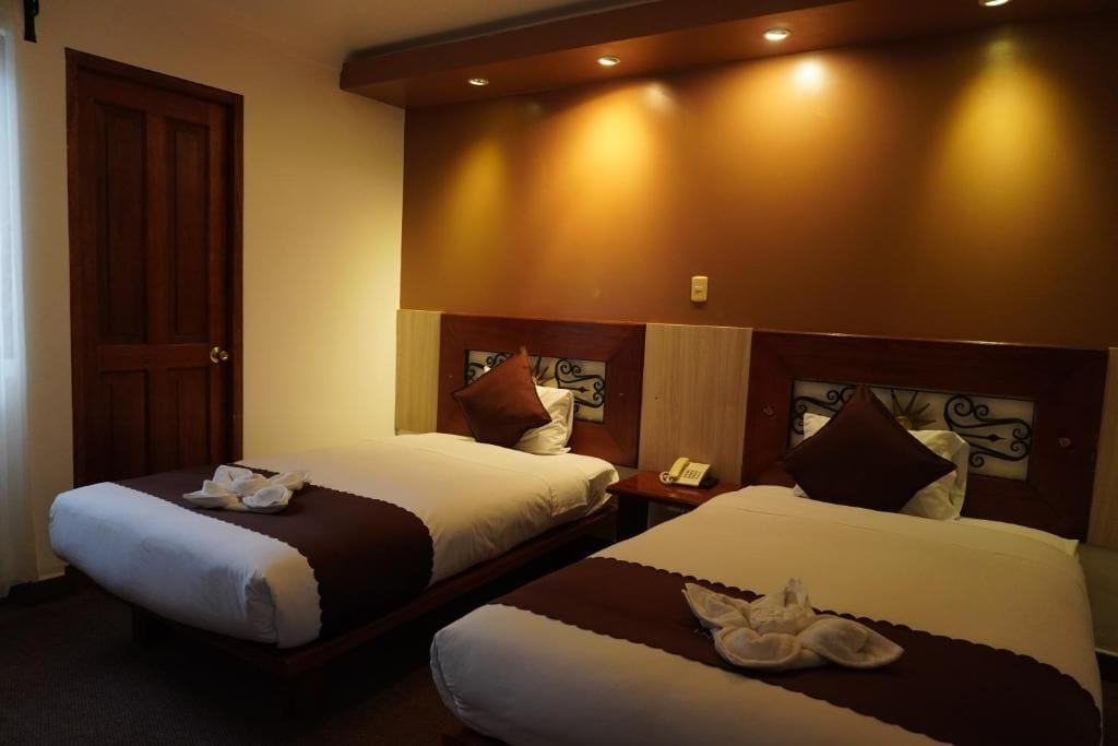 A hotel room with two beds, each with a pillow and a blanket. There is a wooden door and a wall-mounted telephone.