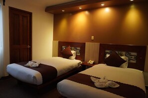A hotel room with two beds, each with a pillow and a blanket. There is a wooden door and a wall-mounted telephone. - INTI MAGIC EL TAMBO (Aguas Calientes)