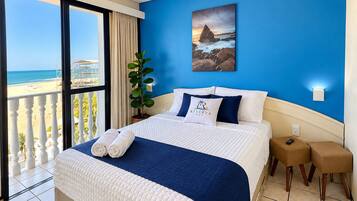 Een hotelkamer met een bed, uitzicht op het strand en een schilderij aan de muur.
