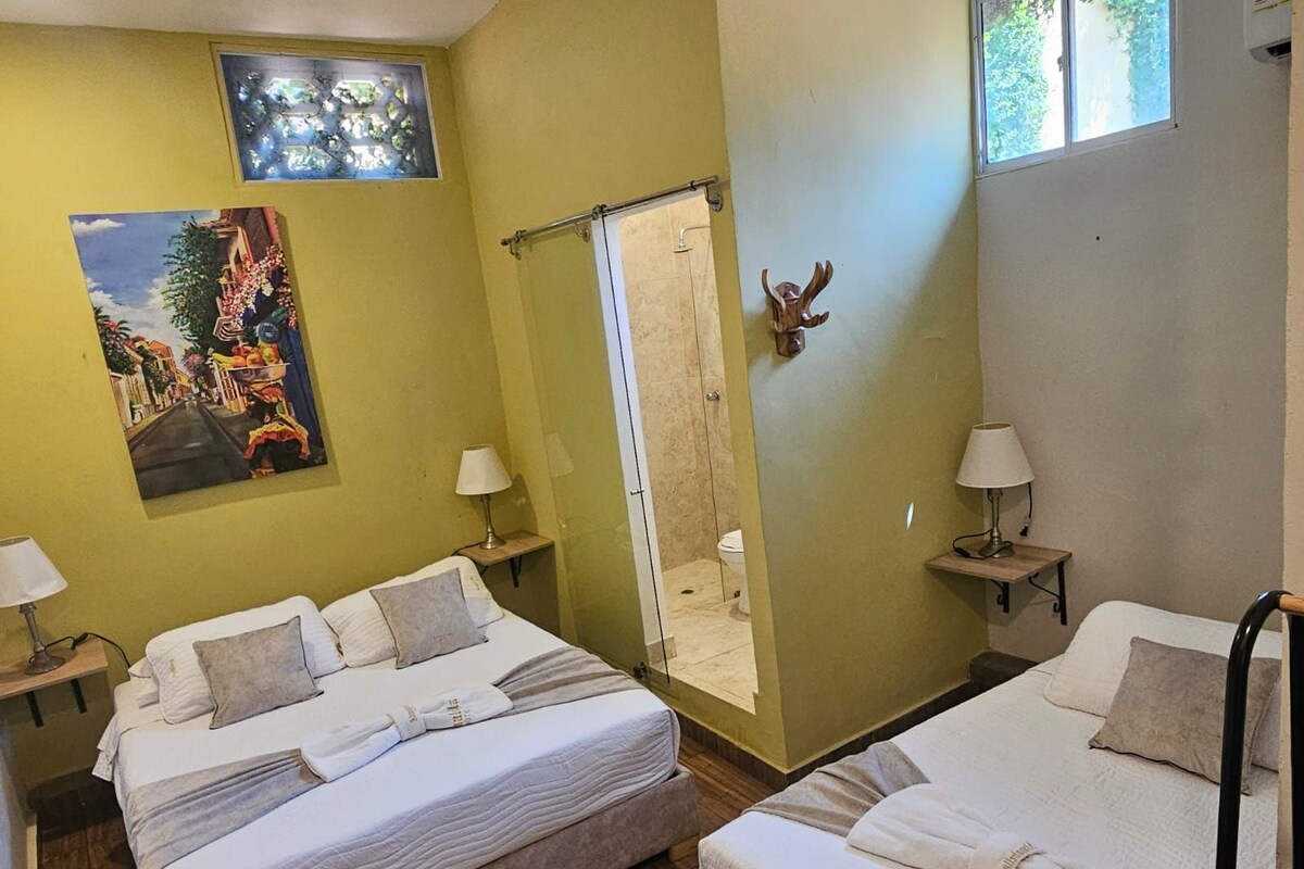 A hotel room with two beds, a shower area, a painting on the wall, and a window with a view.