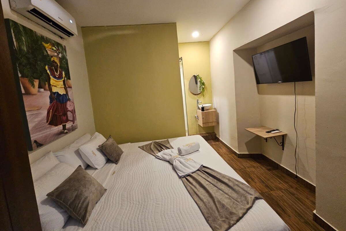 A hotel room with a bed, a television, a painting, and a small bathroom area.