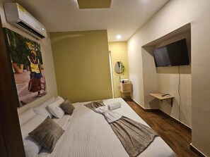 A hotel room with a bed, a television, a painting, and a small bathroom area. - Hotel Almabella (Cartagena de Indias)
