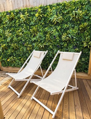 Två vita loungestolar på ett trädäck med en grön häck som bakgrund.