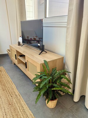 En möbel i trä som används för förvaring och underhållning, med en platt-TV, en flätad korg och en krukväxt.