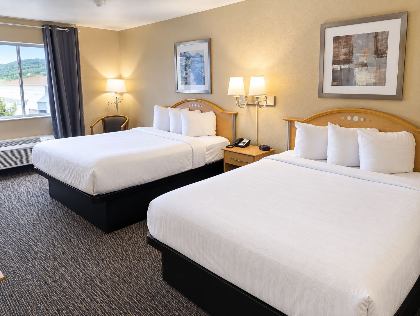 Une chambre d’hôtel avec deux lits, une chaise, un bureau avec un téléphone et deux lampes fixées au mur.
