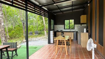 A covered outdoor area with a dining table and chairs, a fan, and a view of the surrounding greenery.