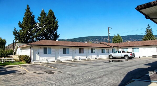 A motel with a single-story structure, a parking lot, and a mountain backdrop. - Ranchland Villa Motel (Merritt)