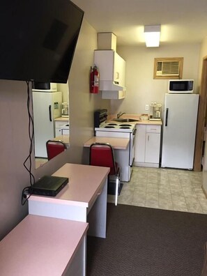 A compact kitchen with a microwave, stove, and refrigerator. There is a small dining area with a table and chairs. - Ranchland Villa Motel (Merritt)