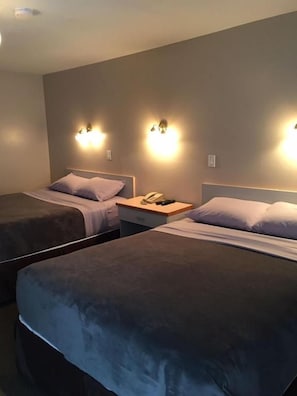 A hotel room with two beds, bedside lamps, a nightstand, and a phone. - Ranchland Villa Motel (Merritt)