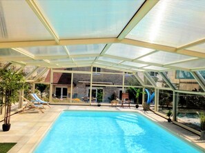 En swimmingpool med et glasafskærmning, omgivet af liggestole og plantekasser.