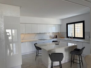 Une cuisine moderne avec des meubles blancs, un îlot central doté de tabourets de bar et une fenêtre à motifs géométriques.