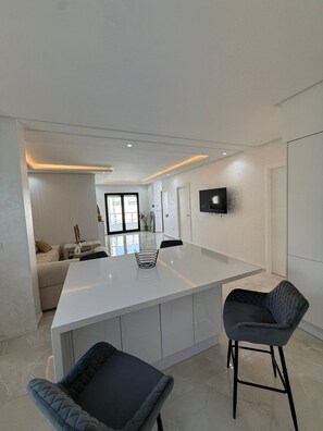 A modern kitchen with a large island, bar stools, and a flat-screen TV mounted on the wall. - New Listing (Marsa)
