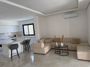 Un salon moderne avec un canapé, une table basse et un coin repas comprenant des chaises, et une cuisine en arrière-plan.