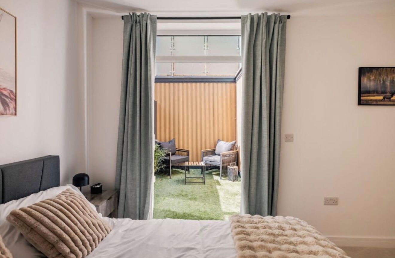 Une chambre à coucher comprenant un lit, une table de chevet, une lampe et donnant sur une terrasse extérieure avec un canapé et une table.