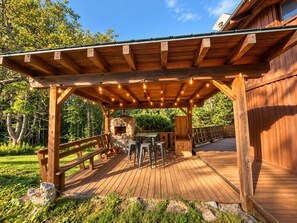 A wooden deck with a pergola, outdoor seating, and a stone fireplace.