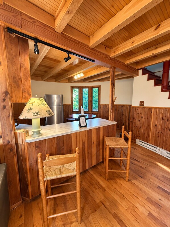 A wooden interior with a kitchen area, a dining table with chairs, and a staircase.
