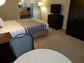 A hotel room with a bed, a desk, a chair, a television, and a wardrobe. - Wild Rose Country Inn (Grande Prairie)
