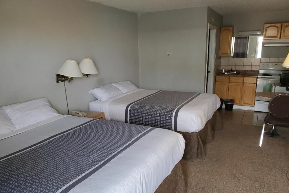 A hotel room with two beds, a kitchenette, and a bathroom.