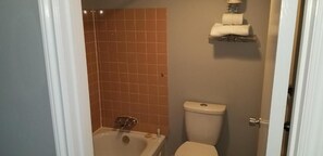 A bathroom with a bathtub, toilet, and a shelf with towels. - Wild Rose Country Inn (Grande Prairie)