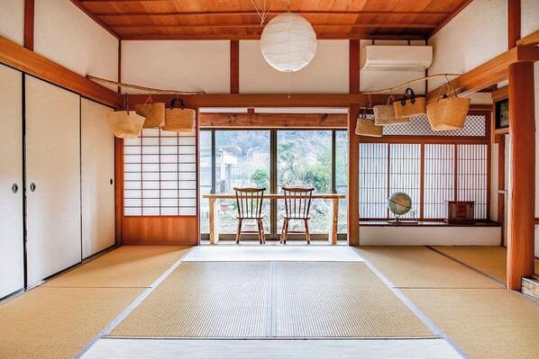 A traditional Japanese room with tatami flooring, a shoji screen door, a wooden table with chairs, and hanging baskets. - Mountain Home - One Hour from Osaka (Uda)