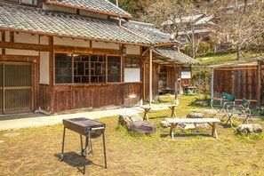 A traditional Japanese building with a tiled roof, wooden exterior, and a small outdoor seating area with benches and a grill. - Mountain Home - One Hour from Osaka (Uda)