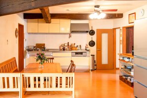 A compact kitchen with wooden cabinets, a dining table with chairs, and a refrigerator. - Mountain Home - One Hour from Osaka (Uda)