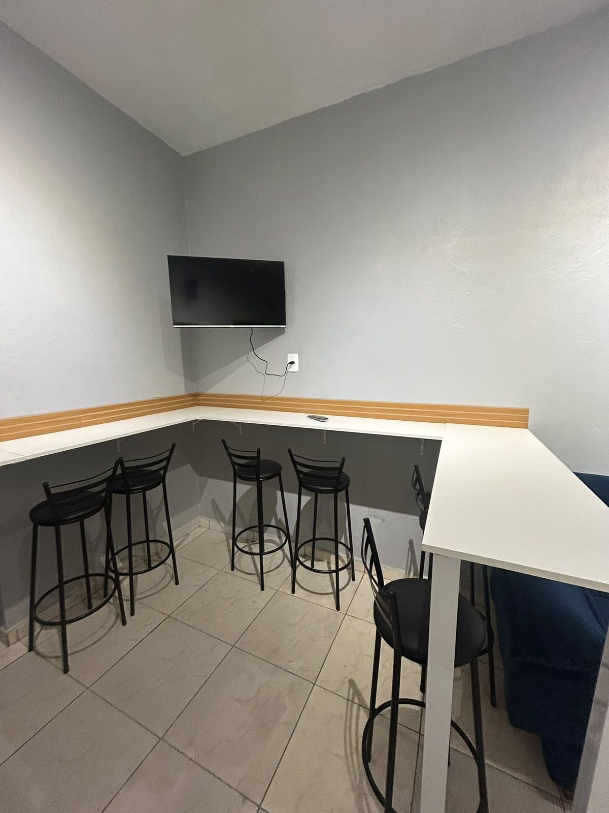 Een kamer met een witte tafel en vier zwarte stoelen, een aan de muur bevestigde flatscreen-tv en een betegelde vloer.