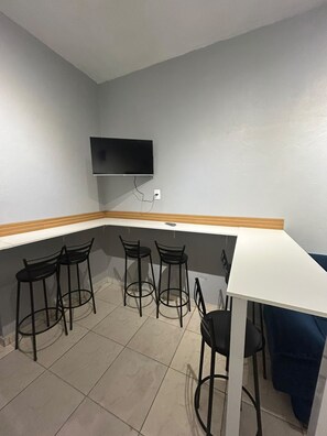 A room with a white table and four black chairs, a flat-screen TV mounted on the wall, and a tiled floor. - New Listing (Jaraguá do Sul)