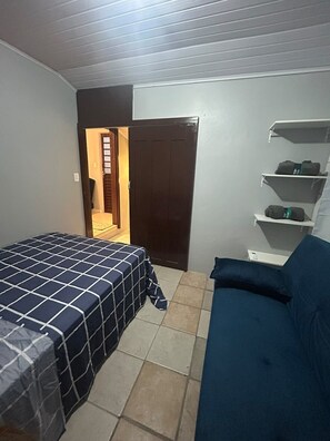 A bedroom with a bed, a sofa, a wardrobe, and a shelf with items. - New Listing (Jaraguá do Sul)