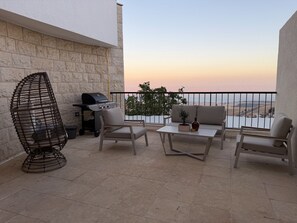 Une terrasse extérieure avec un mur en pierre, un barbecue, une chaise en osier et un canapé.