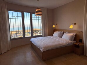 Une chambre d’hôtel avec un grand lit, deux lampes de chevet, une table de nuit et une vue sur un paysage par la fenêtre.