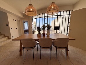 Un coin repas avec une longue table en bois, trois chaises et deux lampes en osier suspendues.